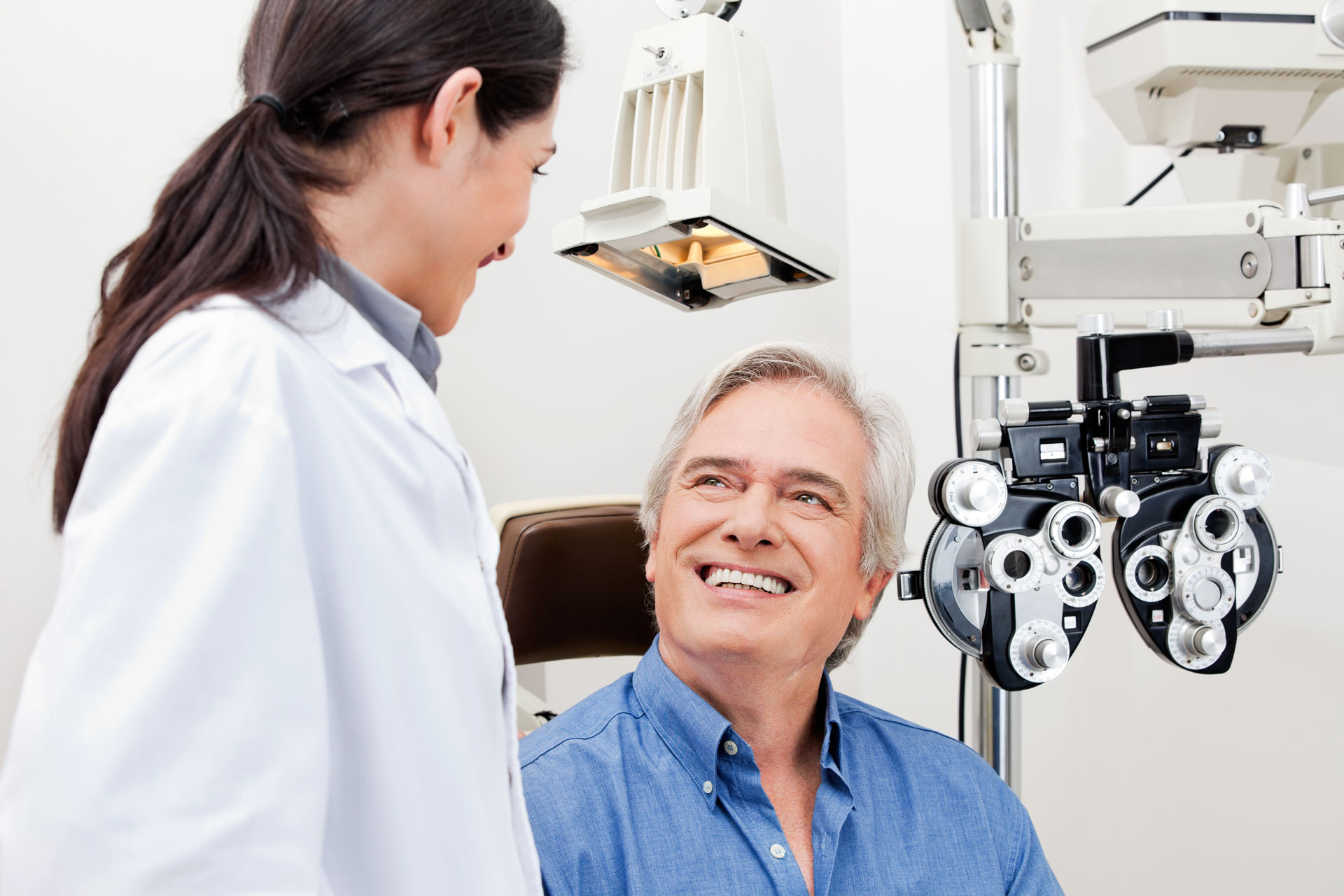 Older man smiling at female optometrist during eye exam